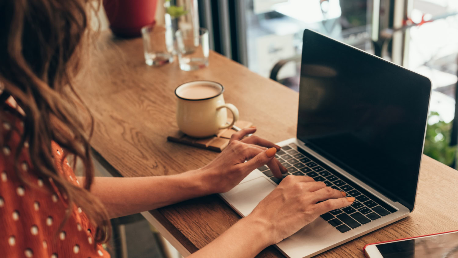 Bild einer jungen, rothaarigen Frau, die in einem Café sitzt und an einem Laptop an ihrem Blog schreibt.